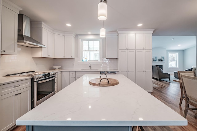 kitchen with stainless steel range with electric stovetop, wall chimney exhaust hood, decorative light fixtures, hardwood / wood-style floors, and plenty of natural light