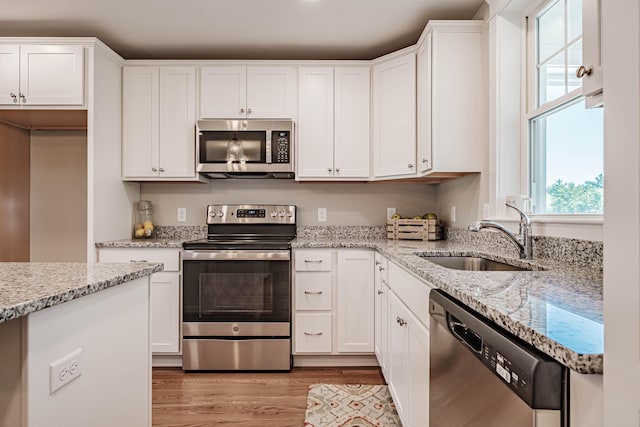 kitchen with white cabinets, sink, light wood-type flooring, light stone countertops, and stainless steel appliances