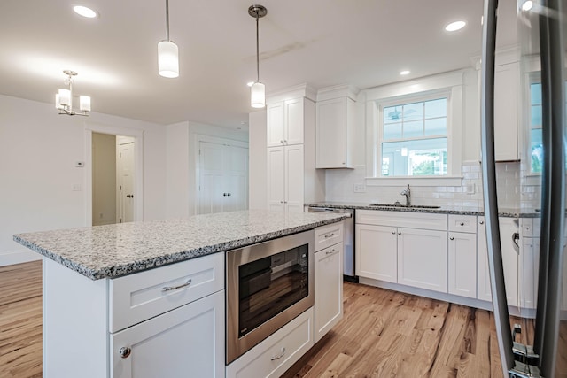 kitchen with sink, stainless steel microwave, pendant lighting, white cabinets, and light wood-type flooring