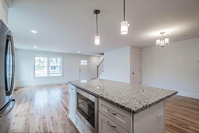 kitchen with appliances with stainless steel finishes, light wood-type flooring, decorative light fixtures, a notable chandelier, and white cabinets