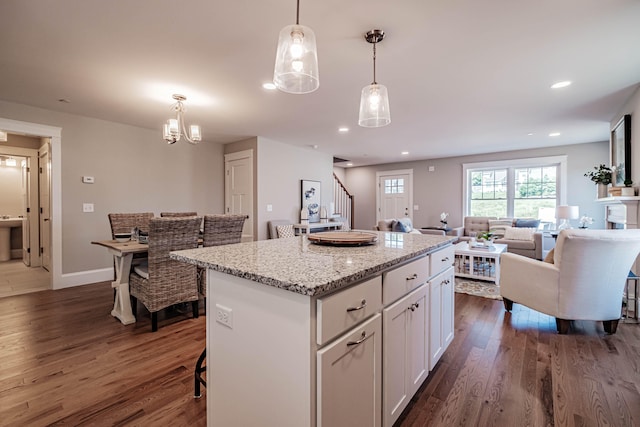 kitchen with light stone countertops, a kitchen island, dark wood-type flooring, pendant lighting, and white cabinetry