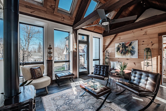 living area with wood walls, high vaulted ceiling, a skylight, ceiling fan, and beam ceiling