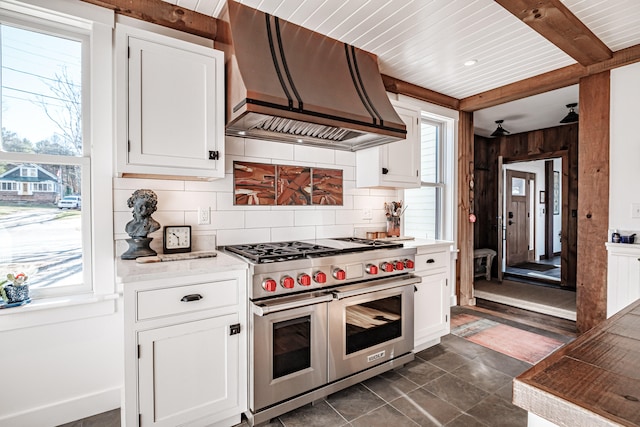 kitchen with tasteful backsplash, custom exhaust hood, dark tile patterned flooring, range with two ovens, and white cabinetry