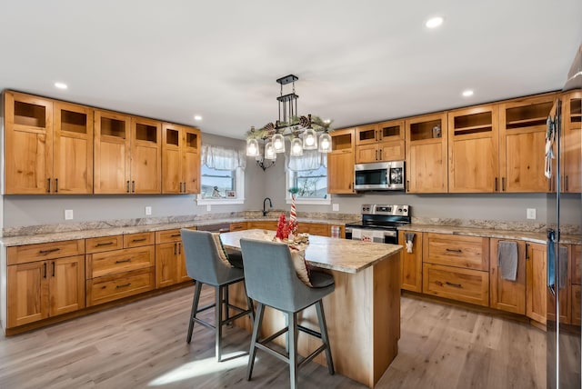 kitchen with light stone countertops, light wood-type flooring, a breakfast bar, stainless steel appliances, and a center island