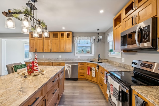 kitchen featuring sink, light stone counters, light hardwood / wood-style floors, decorative light fixtures, and appliances with stainless steel finishes