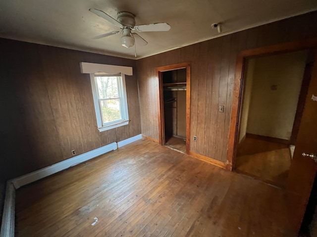 unfurnished bedroom with wooden walls, a closet, ceiling fan, and wood-type flooring