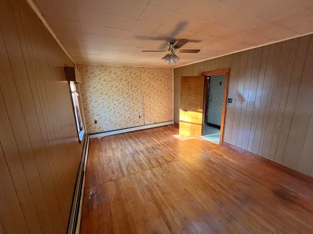 spare room with hardwood / wood-style floors, a baseboard radiator, ceiling fan, and wood walls