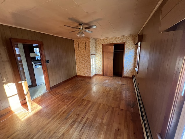 23 Hillcrest Ave, Millinocket, ME 04462 - empty room with light wood-style flooring, a ceiling fan, a baseboard heating unit, plenty of natural light, and wooden walls