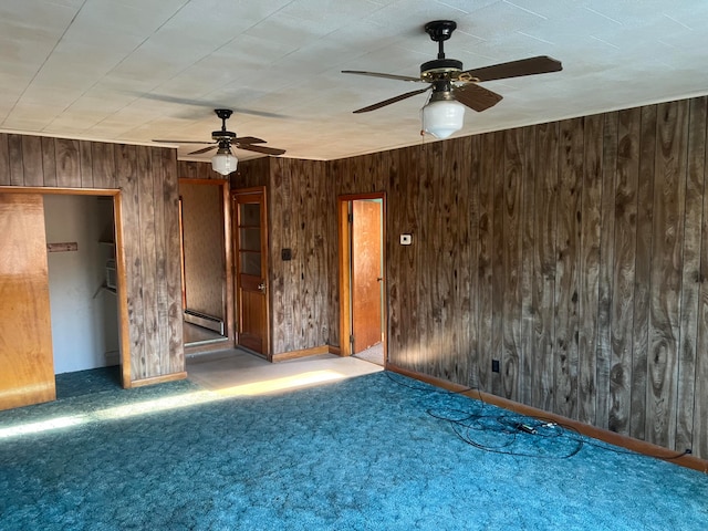 carpeted spare room featuring ceiling fan, wood walls, and a baseboard radiator