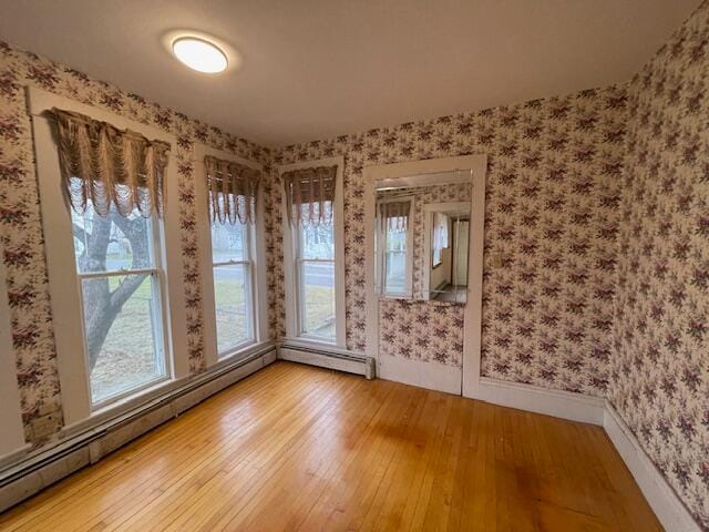 unfurnished room featuring hardwood / wood-style flooring and a baseboard heating unit