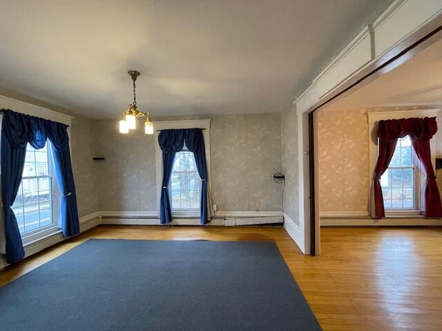 spare room featuring plenty of natural light, hardwood / wood-style floors, a baseboard radiator, and a notable chandelier