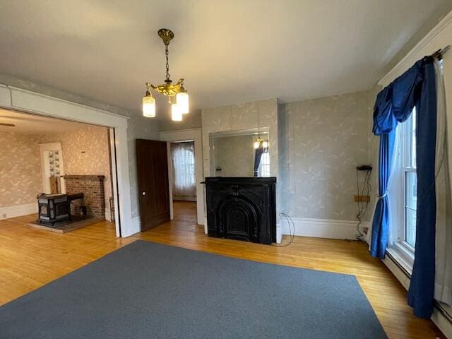 unfurnished living room featuring hardwood / wood-style floors, a notable chandelier, a wood stove, and a baseboard heating unit