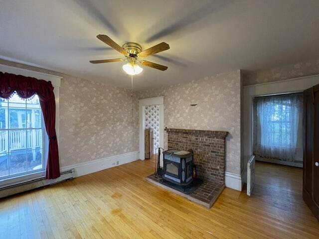 unfurnished living room featuring a wood stove, ceiling fan, wood-type flooring, and a baseboard heating unit