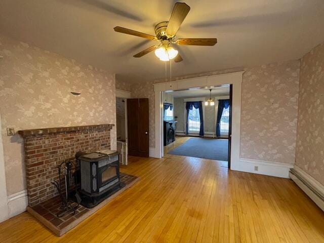 unfurnished living room featuring wood-type flooring, a wood stove, baseboard heating, and ceiling fan