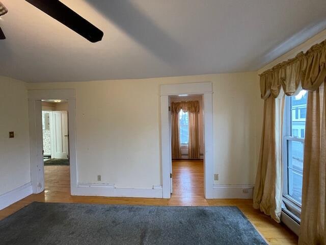 unfurnished room featuring plenty of natural light, a baseboard heating unit, and light wood-type flooring