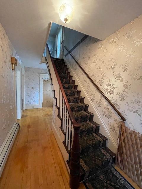 stairway with hardwood / wood-style floors and a baseboard heating unit