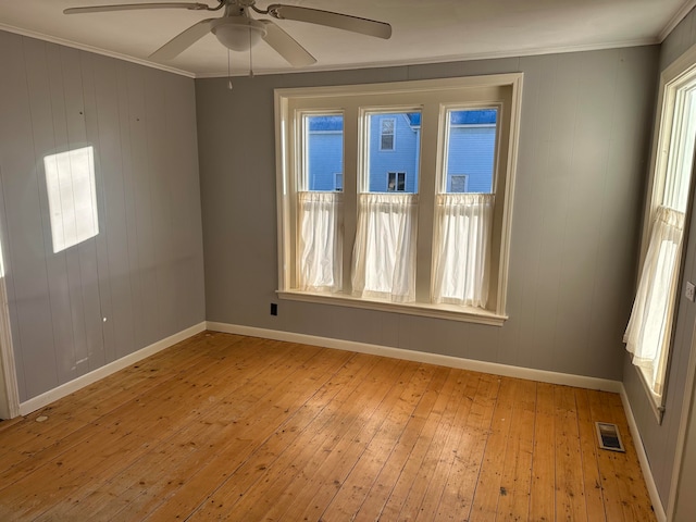 spare room with crown molding, wooden walls, ceiling fan, and light wood-type flooring