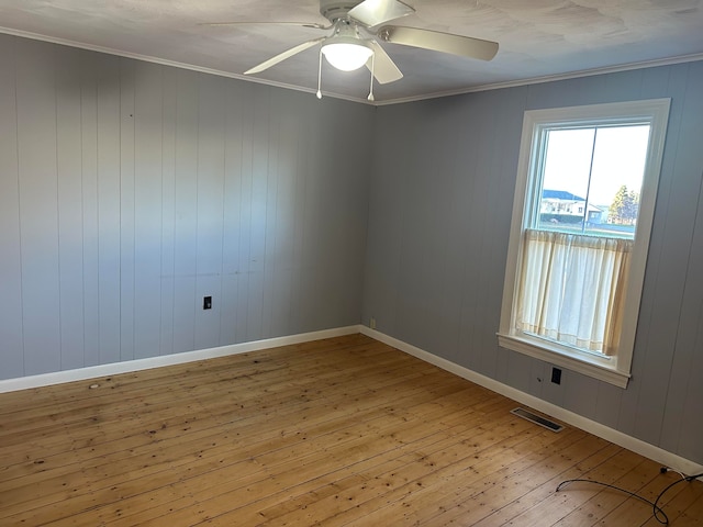 spare room featuring wooden walls, light hardwood / wood-style flooring, ceiling fan, and crown molding