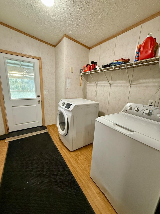 clothes washing area with crown molding, light wood-type flooring, a textured ceiling, and separate washer and dryer