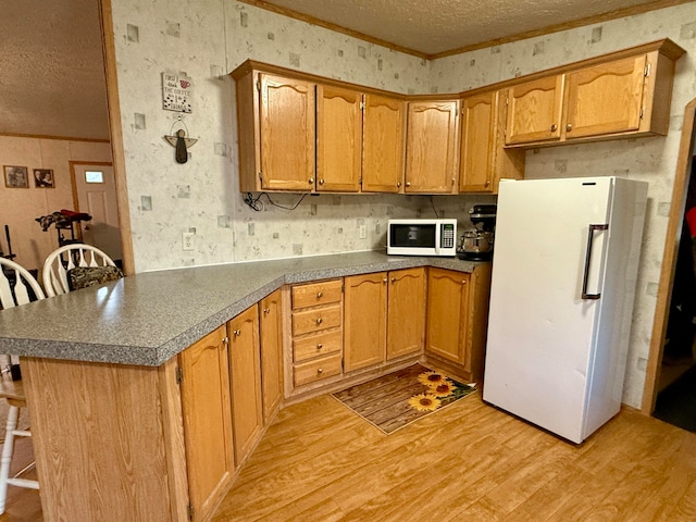 kitchen with white appliances, crown molding, light hardwood / wood-style flooring, a textured ceiling, and a kitchen bar