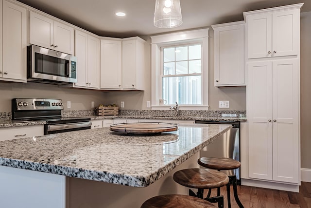 kitchen with white cabinets, appliances with stainless steel finishes, decorative light fixtures, and dark wood-type flooring