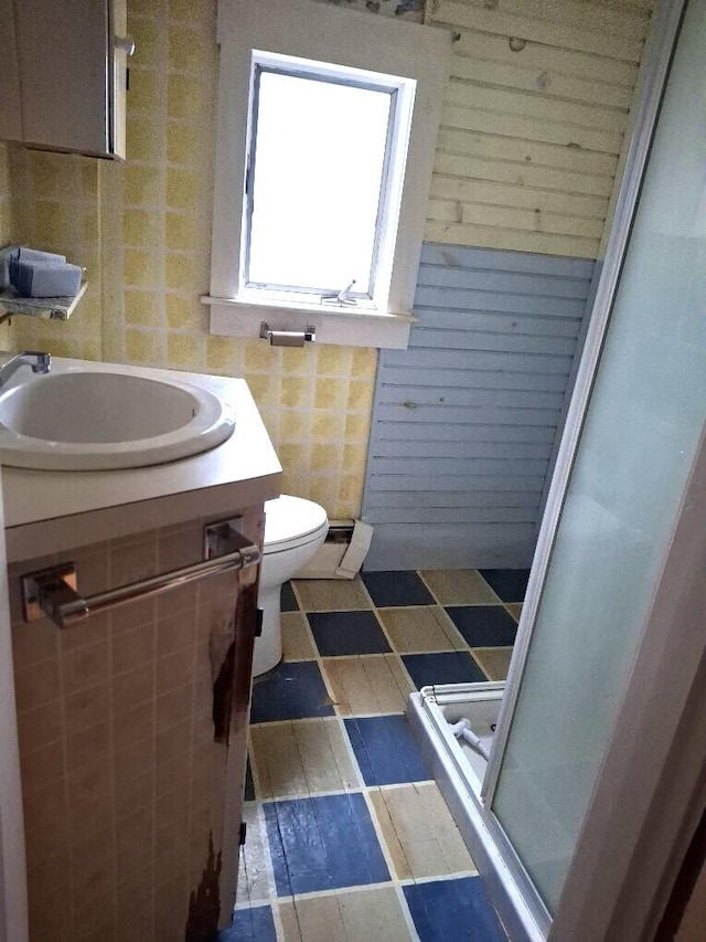 bathroom featuring vanity, toilet, walk in shower, and tile walls