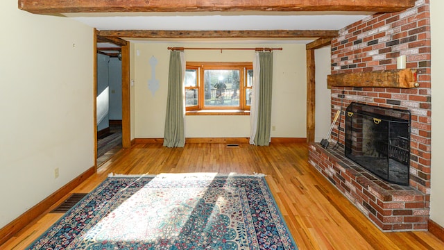 unfurnished living room with light hardwood / wood-style flooring, beamed ceiling, and a brick fireplace