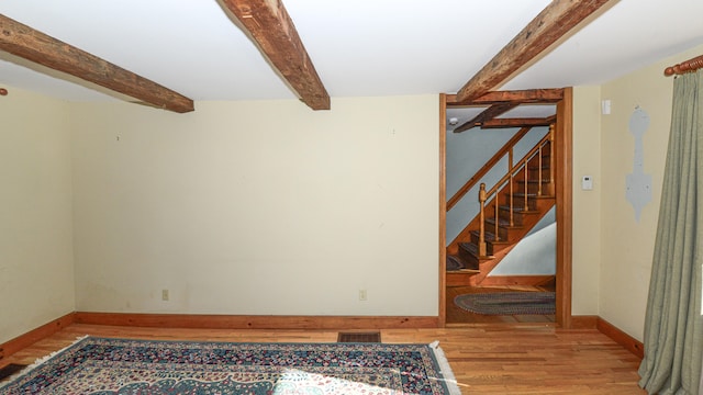 spare room featuring beam ceiling and light hardwood / wood-style flooring