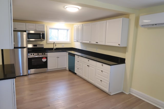 kitchen with appliances with stainless steel finishes, a wall unit AC, sink, white cabinets, and light hardwood / wood-style floors