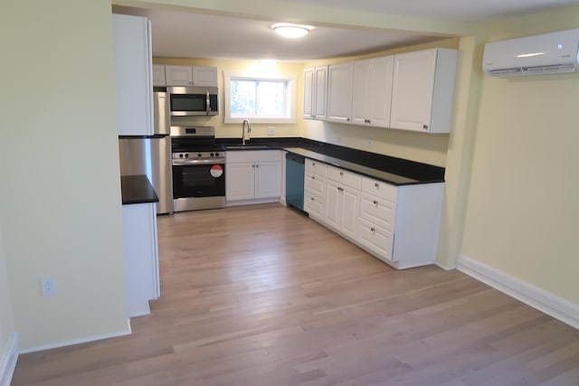 kitchen with appliances with stainless steel finishes, light wood-type flooring, sink, an AC wall unit, and white cabinets