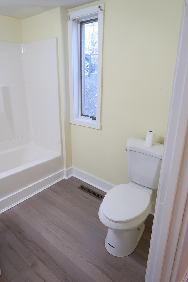 bathroom featuring washtub / shower combination, wood-type flooring, and toilet