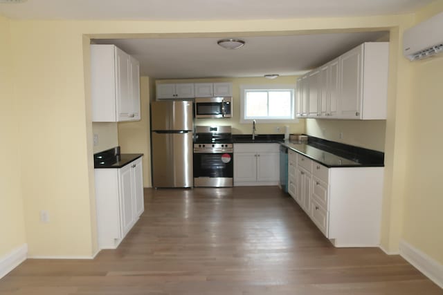 kitchen with appliances with stainless steel finishes, sink, wood-type flooring, an AC wall unit, and white cabinetry