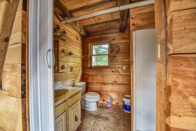 bathroom featuring beam ceiling, wooden walls, vanity, and toilet