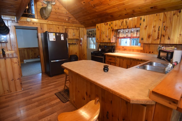 kitchen with kitchen peninsula, vaulted ceiling, sink, black appliances, and wood-type flooring