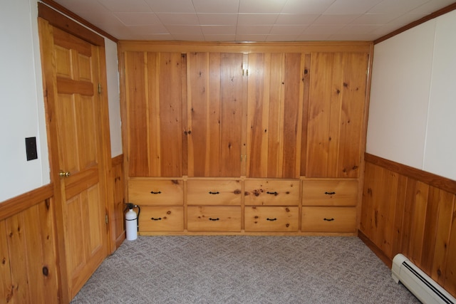 carpeted empty room with a baseboard heating unit and wood walls