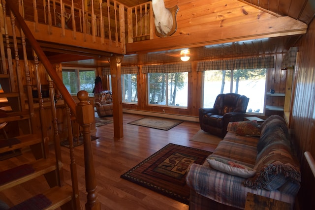 living room with wood-type flooring, wooden walls, a baseboard radiator, and lofted ceiling