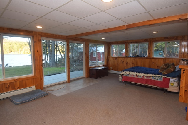 bedroom with a drop ceiling, baseboard heating, multiple windows, and wooden walls