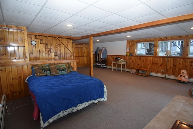 bedroom featuring wood walls, a drop ceiling, and dark carpet