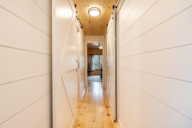 hall with a barn door, wooden ceiling, light hardwood / wood-style flooring, and wooden walls