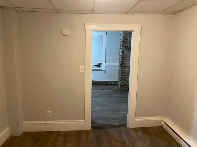 empty room with dark wood-type flooring, a baseboard radiator, and a drop ceiling