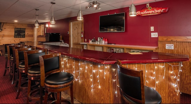 bar featuring carpet flooring, black fridge, wood walls, pendant lighting, and a paneled ceiling