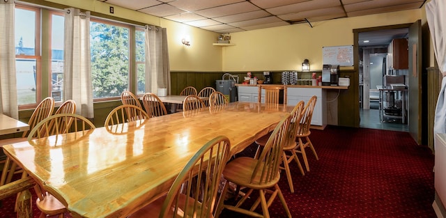 dining space featuring a paneled ceiling, wood walls, and a water view