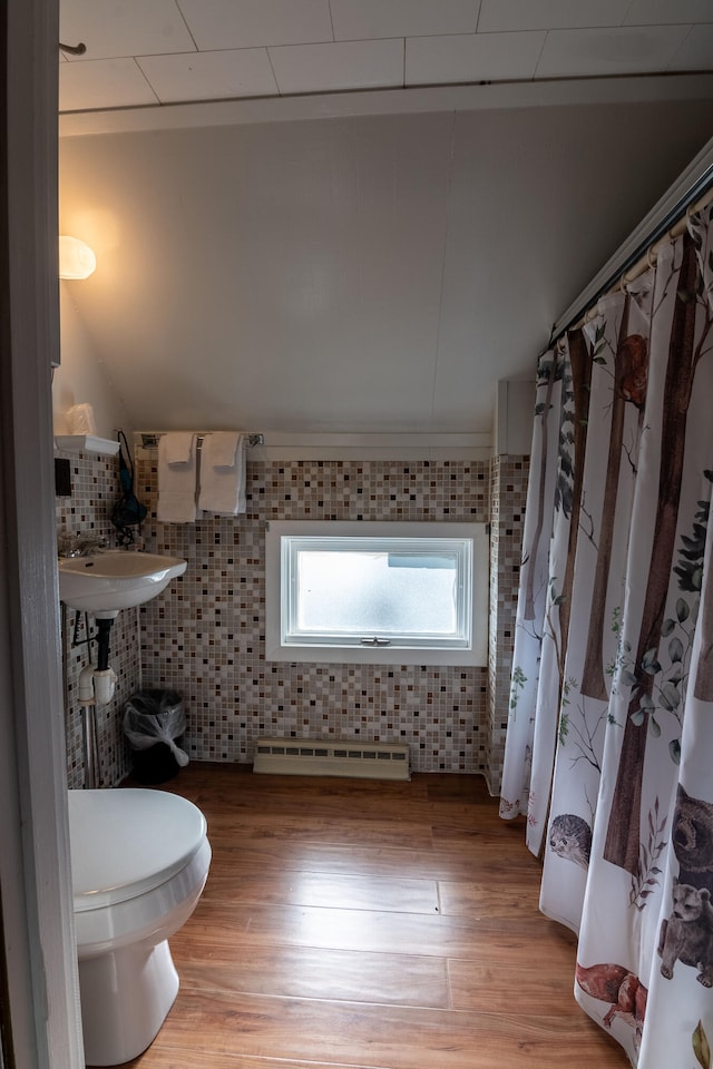 bathroom with toilet, wood-type flooring, tile walls, and a baseboard heating unit