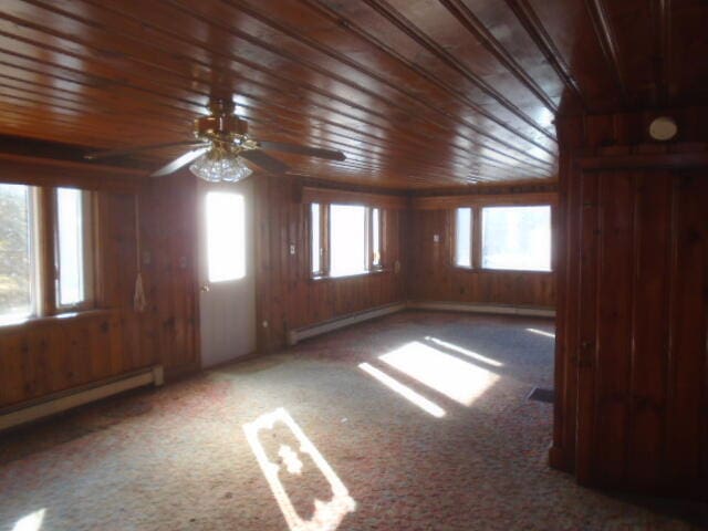 empty room featuring carpet, baseboard heating, ceiling fan, and a healthy amount of sunlight