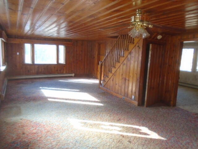 empty room featuring ceiling fan, wooden walls, and a baseboard radiator