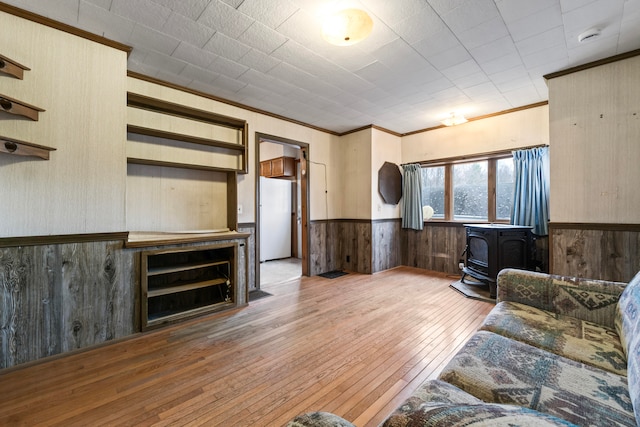 living room with hardwood / wood-style flooring, a wood stove, ornamental molding, and wooden walls