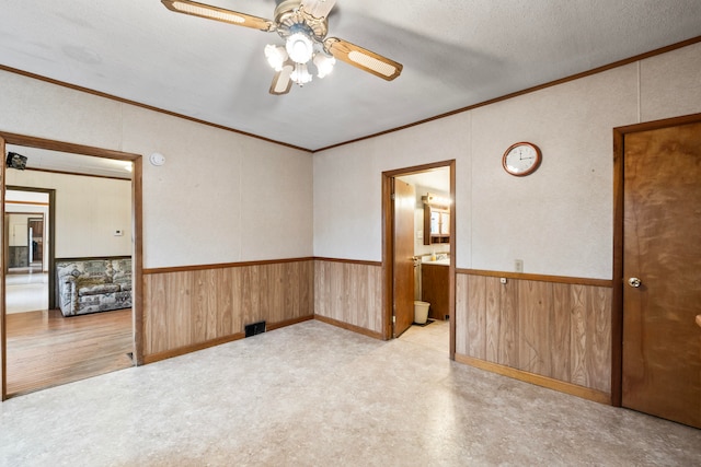 empty room featuring ceiling fan, wood walls, crown molding, and a textured ceiling