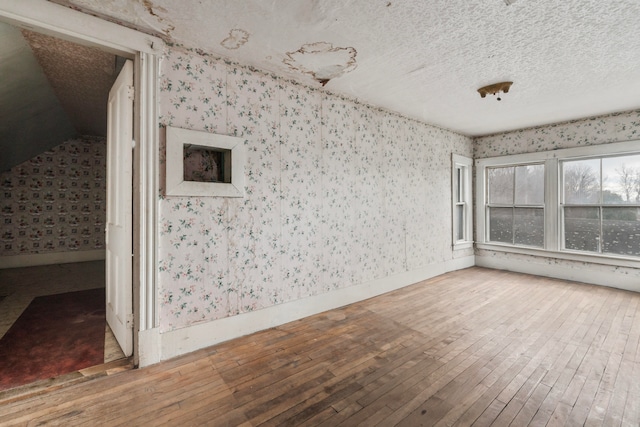 unfurnished room featuring hardwood / wood-style floors, a textured ceiling, and vaulted ceiling