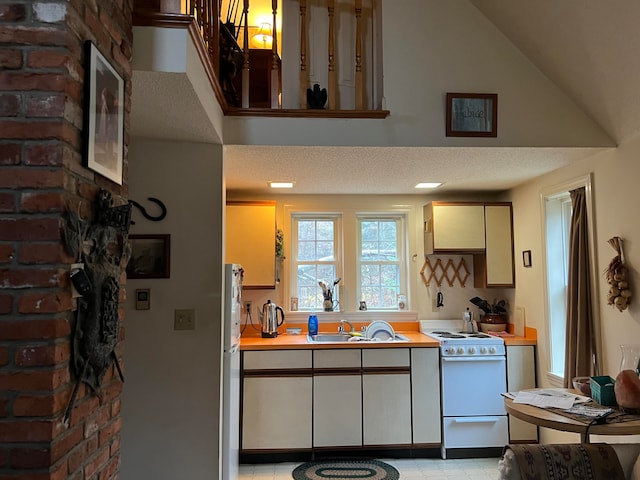 kitchen with white range, sink, vaulted ceiling, stainless steel fridge, and a textured ceiling