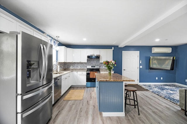 kitchen with a center island, hanging light fixtures, appliances with stainless steel finishes, light hardwood / wood-style floors, and a wall unit AC